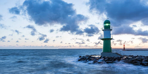 Germany, Mecklenburg-West Pomerania, Warnemunde, Lighthouse and sea waves crashing against rocks at dusk - WDF05722