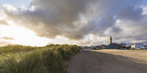 Germany, Mecklenburg-West Pomerania, Warnemunde, Grass on sand dunes and lighthouse at sunset stock photo