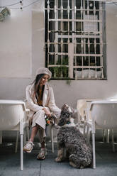 Junge Frau sitzt mit ihrem Hund in einem Café in der Stadt - GRCF00137