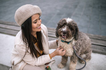 Happy young woman stroking her dog in the city - GRCF00138