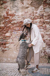 Glückliche junge Frau spielt mit ihrem Hund in der Stadt - GRCF00141
