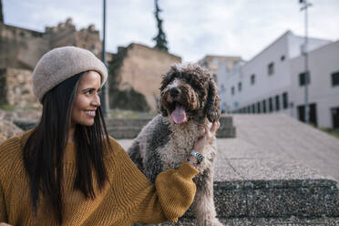 Happy young woman stroking her dog in the city - GRCF00145