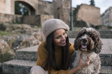 Happy young woman stroking her dog in the city - GRCF00146