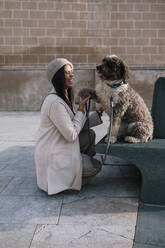 Lachende junge Frau mit ihrem Hund in der Stadt, der Pfötchen gibt - GRCF00152