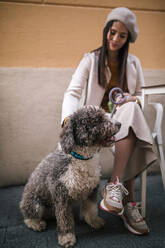 Junge Frau sitzt mit ihrem Hund in einem Café in der Stadt - GRCF00155