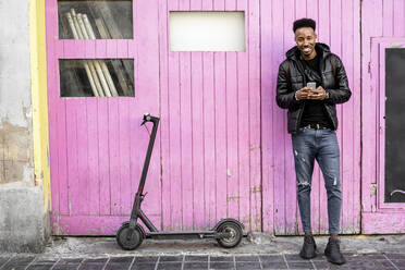 Portrait of smiling man with smartphone and e-scooter outdoors - RCPF00213