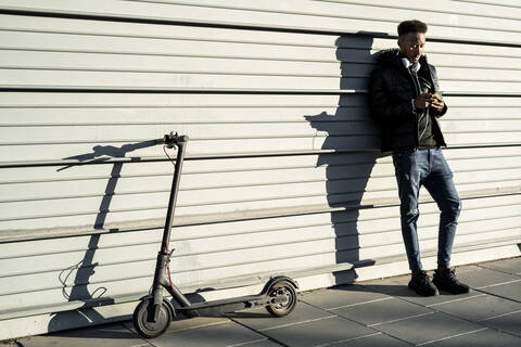 Man with smartphone and e-scooter outdoors stock photo