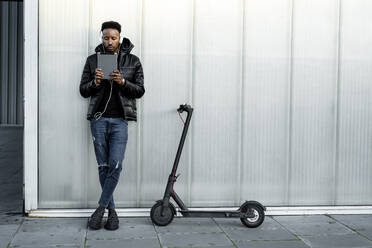 Man with headphones, tablet and e-scooter outdoors - RCPF00219
