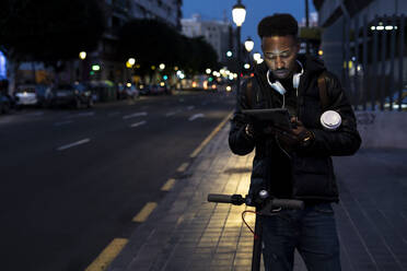 Mann in der Stadt bei Nacht mit Tablet und E-Scooter - RCPF00225