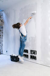 Girl jumping while painting a wall in a house - DGOF00206