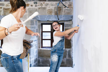Mother and daughter having fun while painting a wall of her new house - DGOF00209