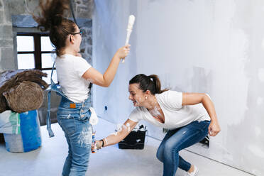 Playful mother and daughter having fun while painting a wall of her new house - DGOF00213