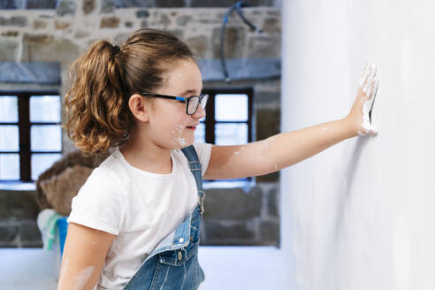 Mädchen mit Farbe an der Hand, das eine Hauswand berührt - DGOF00218