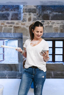 Frau benutzt ihr Handy beim Streichen der Wände ihres neuen Hauses - DGOF00243
