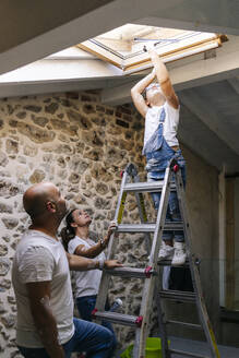 Eltern beobachten ihre Tochter beim Putzen des Dachfensters - DGOF00245