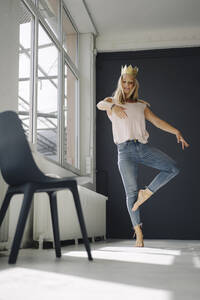 Blonde junge Frau mit einer Krone tanzt in einem Loft - KNSF07378
