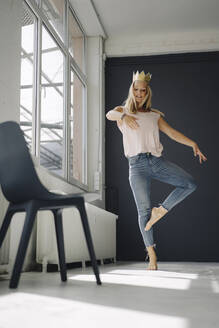 Blond young woman wearing a crown dancing in a loft - KNSF07378