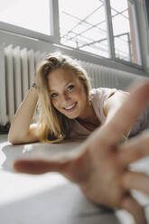 Porträt einer glücklichen blonden jungen Frau, die auf dem Boden liegt - KNSF07386