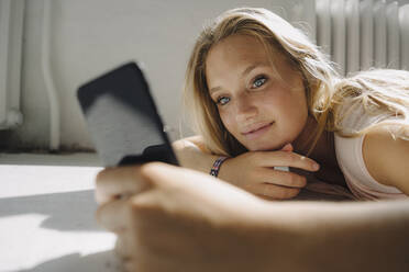 Blond young woman lying on the floor using cell phone - KNSF07388