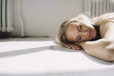 Porträt einer blonden jungen Frau, die mit geschlossenen Augen auf dem Boden liegt - KNSF07389