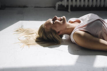 Lächelnde blonde junge Frau auf dem Boden liegend im Sonnenlicht - KNSF07394
