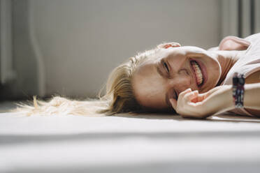 Porträt einer glücklichen blonden jungen Frau, die mit geschlossenen Augen auf dem Boden liegt - KNSF07396
