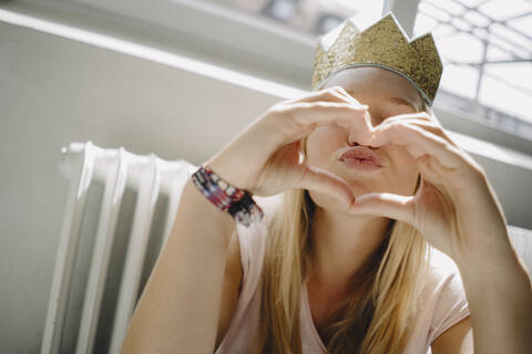 Young woman wearing a crown shaping a heart with her hands stock photo