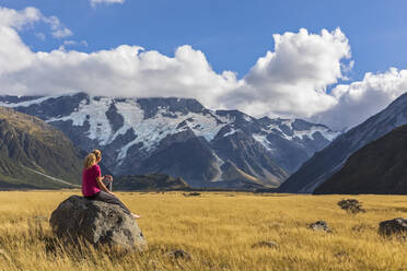 Neuseeland, Ozeanien, Südinsel, Canterbury, Ben Ohau, Südliche Alpen (Neuseeländische Alpen), Mount Cook National Park, Aoraki / Mount Cook, Frau sitzt auf Felsblock in Berglandschaft - FOF11657