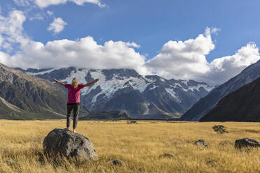 Neuseeland, Ozeanien, Südinsel, Canterbury, Ben Ohau, Südliche Alpen (Neuseeländische Alpen), Mount Cook National Park, Aoraki / Mount Cook, Frau steht auf Felsblock in Berglandschaft - FOF11658