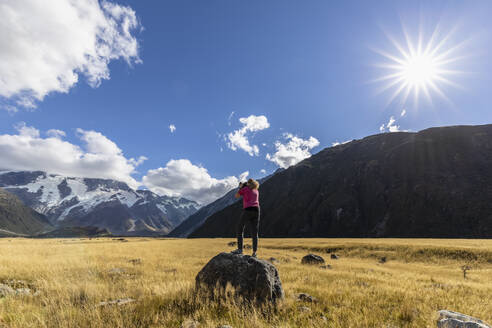 Neuseeland, Ozeanien, Südinsel, Canterbury, Ben Ohau, Südliche Alpen (Neuseeländische Alpen), Mount Cook National Park, Aoraki / Mount Cook, Frau steht auf Felsblock und fotografiert Berglandschaft - FOF11662