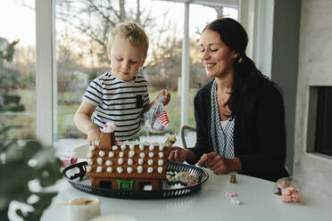 Mutter mit Sohn beim Bau eines Lebkuchenhauses - JOHF06548