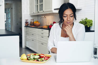 Woman using laptop in kitchen - JOHF06612