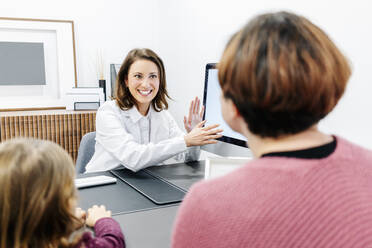 Arzt im Gespräch mit Mutter mit Tochter am Schreibtisch in einer Arztpraxis - DGOF00251