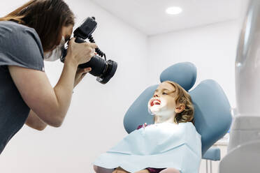 Dentist taking picture of girl receiving dental treatment - DGOF00262