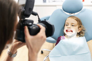 Dentist taking picture of girl receiving dental treatment - DGOF00263