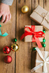 Frau wickelt Weihnachtsgeschenke auf hölzernem Hintergrund ein - CAVF73691