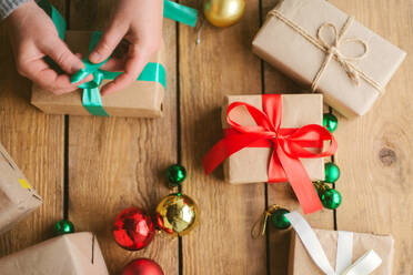 Frau wickelt Weihnachtsgeschenke auf hölzernem Hintergrund ein - CAVF73692