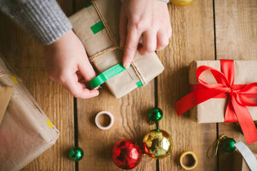 Frau wickelt Weihnachtsgeschenke auf hölzernem Hintergrund ein - CAVF73693