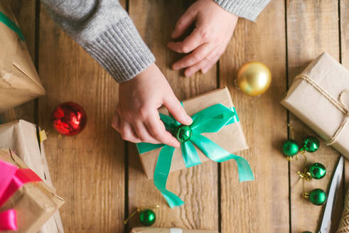 Frau wickelt Weihnachtsgeschenke auf hölzernem Hintergrund ein - CAVF73694