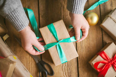 Frau wickelt Weihnachtsgeschenke auf hölzernem Hintergrund ein - CAVF73695