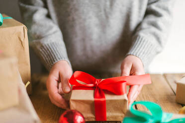 Frau wickelt Weihnachtsgeschenke auf hölzernem Hintergrund ein - CAVF73696