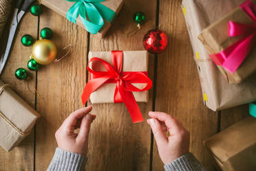 Frau wickelt Weihnachtsgeschenke auf hölzernem Hintergrund ein - CAVF73697