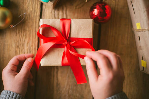 Frau wickelt Weihnachtsgeschenke auf hölzernem Hintergrund ein - CAVF73698