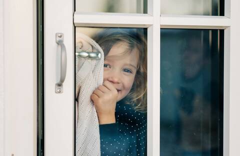 Young girl looking through a door window smiling looking happy stock photo