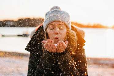 Frau bläst goldenen Schnee bei Sonnenuntergang im Winter - CAVF73735