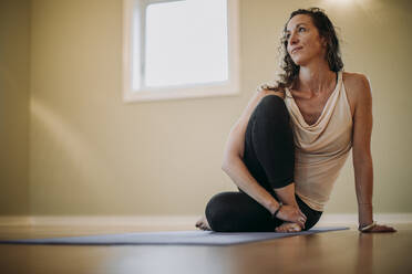 Barefoot woman relaxes on yoga mat in an indoor studio - CAVF73807