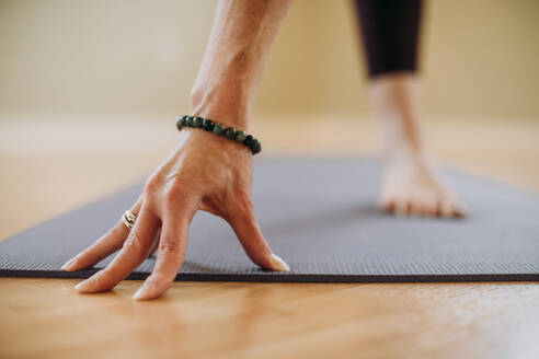 Close up weibliche Hand mit Armband und nackten Fuß auf Yoga-Matte im Studio - CAVF73809