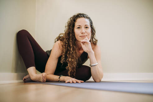 Fit Frau mit lockigem Haar entspannt auf Yoga-Matte in der Ecke des Studios - CAVF73810