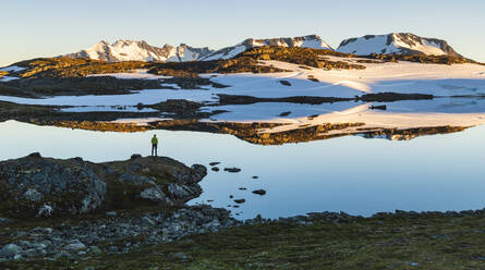 Person standing by lake in mountains - JOHF06914