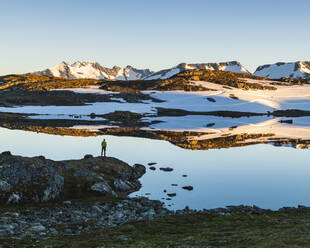 Person standing by lake in mountains - JOHF06915